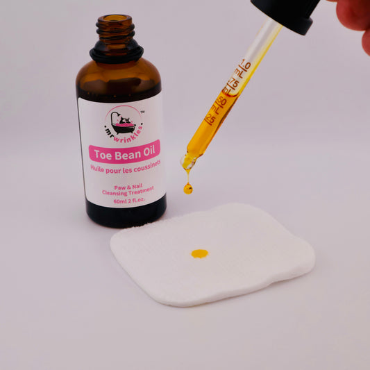 Mr Wrinkles Sphynx Toe Bean Oil Paw and Nail cleansing treatment a drop of oil falling from the dropper towards a cotton pad below